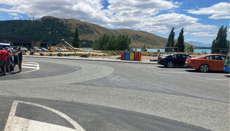 A road with cars parked in front of a lake

Description automatically generated